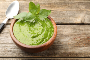 Wall Mural - Tasty green pesto in bowl and basil leaves on wooden table, closeup. Space for text