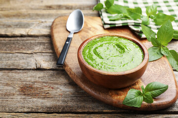 Wall Mural - Tasty green pesto in bowl and basil leaves on wooden table, closeup. Space for text