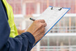 © cunaplus - Hands, engineer and clipboard in city for checklist, inspection notes or safety compliance. Person, writing with documents for urban development, project management or supervisor paperwork and pen