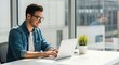 © Glyph Studio - Smiling young man using laptop computer working from home office