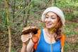 © EdNurg - Woman smiling, holding a bolete mushroom, enjoying foraging during a hike in a natural deciduous forest