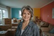 © The 2R Artificiality - Middle-aged woman with grey hair smiling in a newly moved-in home surrounded by boxes and colorful wall paint samples.