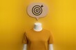© MediaStockAI - A headless mannequin wears a yellow shirt against a yellow backdrop with a speech bubble above containing a target symbol, illustrating focus, goals, and achievements in a creative, conceptual manner.