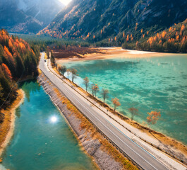 Wall Mural - Aerial view of road, azure lakes, forest in alpine mountains in autumn sunny day. Dolomites, Italy. Travel. Top view of beautiful road, blue water, orange trees in fall. Landscape with highway. Nature