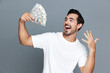 © SHOTPRIME STUDIO - Joyful man celebrating success, holding cash in hands, smiling broadly with excitement. Isolated on plain gray background, studio portrait, lifestyle concept.
