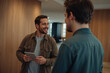 © Masud - Two men smiling and talking in a modern office hallway