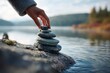 © Chun Sokly - A person stacking rocks on a rock by the water