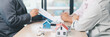 © doidam10 - Mortgage consultation panorama with miniature house model in hand, financial advisor meeting clients, property investment, home loan agreement, real estate planning and housing business negotiation.