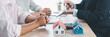 © doidam10 - Mortgage consultation panorama with miniature house model in hand, financial advisor meeting clients, property investment, home loan agreement, real estate planning and housing business negotiation.