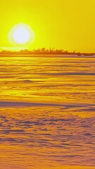 Wall Mural - Vertical time lapse of sunset on the horizon with yellow sky above a snowy field and cloud shadows.
