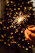 © lunika - bright festive sparkler in mens hands on the background of a christmas tree. the concept of new year holidays and weekends. closeup. selective focus.