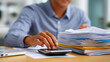 © Kateryna - An accountant prepares tax documents surrounded by files and calculator during busy season wearing business casual attire while carefully reviewing financial statements