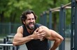 © Pete - Muscular man suffers sharp shoulder pain during intense outdoor gym workout session. Athlete holds sore arm joint after parallel bars exercise. Strong guy experiences severe ache, discomfort from