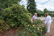 © Ekaterina - Two women nurturing vibrant dahlias and other plants in a home garden, sharing an intergenerational moment while engaged in the enjoyable hobby of horticulture