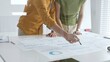 © rogerphoto - Two business professionals are examining financial reports, using a pen to point at specific data points on charts and graphs spread out on a white desk