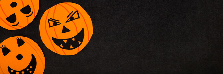 Wall Mural - Orange scary smiling pumpkin faces on dark black table background. Closeup. Creating Halloween decoration. Wide banner. Flat lay. Little child handcraft. Top down view.