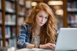 © VolumeThings - Teen girl with red hair using a laptop in the library