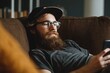 © VolumeThings - Youthful man with a beard relaxing on a sofa while using a smartphone