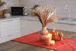 © Pixel-Shot - Vase with pampas grass, autumn decor and burning candles on dining table in kitchen