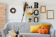 © Pixel-Shot - Interior of light living room decorated for Halloween with grey sofa, shelf unit and broom