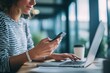 © Alexei - A woman is sitting at her desk using a laptop and cell phone