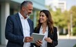 © lan - Mature 40s years old man, young adult woman walking, discussing project on digital pc tablet computer. Successful middle aged latin hispanic businessman, businesswoman work together on business plan