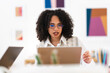 © Studio Marmellata - A young woman with curly hair and glasses works on her laptop in a bright, modern office space with colorful abstract art on the wall.