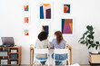 © Studio Marmellata - Two women collaborate on a laptop at a desk in a bright room adorned with colorful abstract art.
