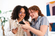 © Studio Marmellata - Two young women with curly hair share a laugh while looking at a smartphone together.