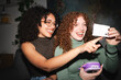 © Studio Marmellata - Two young women with curly hair laugh while looking at a small white card and a purple device.