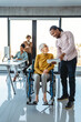 © NDABCREATIVITY - Business woman in wheelchair working with colleague in modern inclusive office. Diversity, support