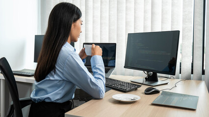 Female programmer holding coffee cup to drinking hot coffee during looking on laptop screen to reading database code