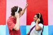 © VISTA by Westend61 - Friends dancing with headphones by a colorful wall in casual outfits