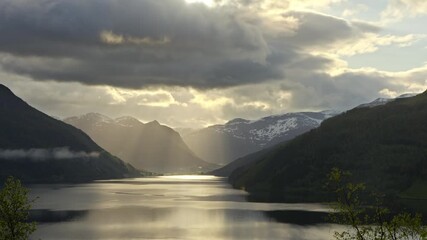 Wall Mural - Timelapse shot of sunrise at Lake Haukedalsvatnet in Norway. The clouds drift gently across the landscape, causing the sun's rays to sparkle on the lake.