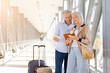 © Anastasiya - Mature couple standing at airport corridor with luggage, reading passports and tickets