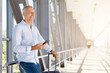© Anastasiya - Happy mature man smiling while holding smartphone at airport corridor with luggage