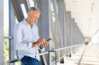 © Anastasiya - Mature man standing at airport corridor with luggage using smartphone