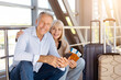© Anastasiya - Mature couple sitting at airport with luggage and passports, smiling at camera
