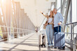 © Anastasiya - Mature couple standing at airport with luggage, pointing aside at copy space