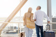 © Anastasiya - Mature couple standing together looking out of airport window with luggage