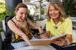 © PintoArt - Mother and daughter with disability laughing together reading notebook