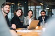 © Manon - A group of four professionals engaged in a meeting, discussing ideas with a laptop on the table, showcasing collaboration and teamwork in a modern office environment.