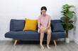 © Ratirat - women suffering from knee pain while sitting on sofa, holding her leg in discomfort. Concept of joint pain, arthritis, muscle injury, or chronic inflammation.