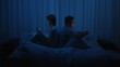 © kinomaster - A couple sits back to back in bed at night using smartphones