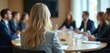 © Maryna - Businesswoman leads meeting with colleagues. Team discuss project around wooden table. Woman in gray blazer speaks to group of people in formal wear.
