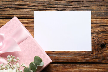 Wall Mural - Blank card, gift box and floral decor on wooden table, flat lay