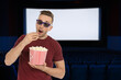 © New Africa - Man with 3D glasses eating popcorn in dark cinema