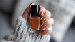 © Newleks - Woman's hand with perfectly painted brown nails holding a matching nail polish bottle, embracing cozy autumn fashion, beauty and self care