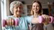 © Johannes - old woman training with physiotherapist using dumbbells at home therapist assisting senior woman with exercises in nursing home elderly patient using dumbbells with outstretched arms no logos no bran
