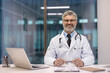 © Liubomir - Mature doctor professional sitting at clinic desk smiling
